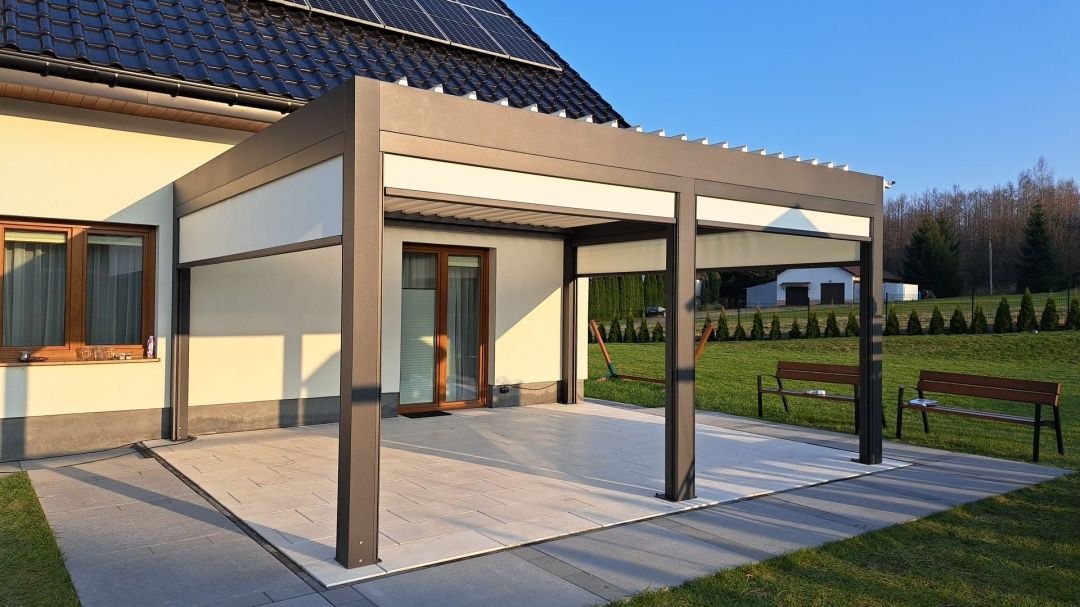 Pergolă bioclimatică din aluminiu lipită de casă, cu închideri laterale tip Screen coborâte parțial peste terasă